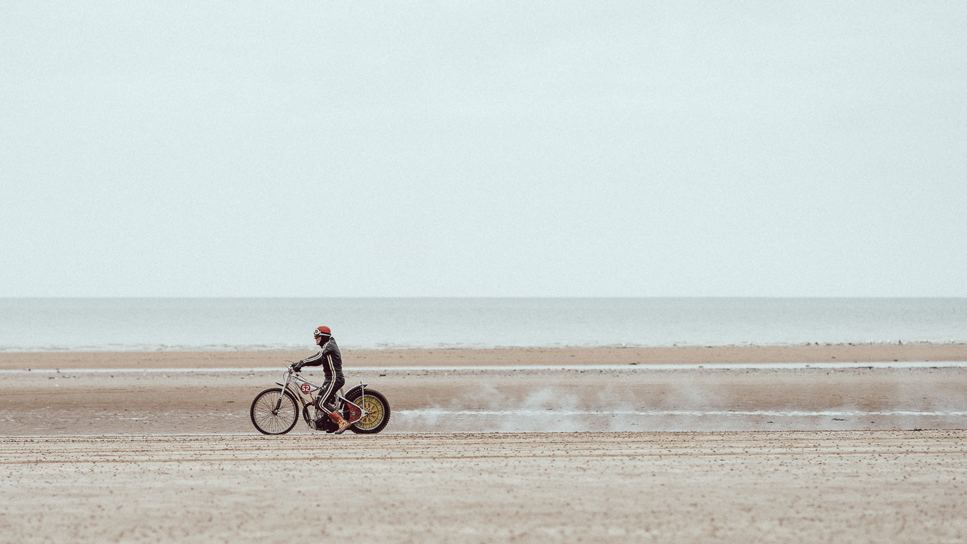 Person riding a bicycle on a sandy beach with a vast ocean and sky in the background